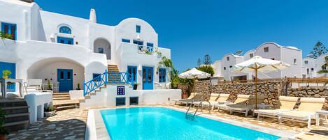 A pool area with a clear blue pool, white buildings with blue accents, and outdoor seating.