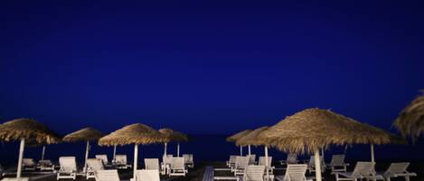 A beach with white lounge chairs and thatched umbrellas.