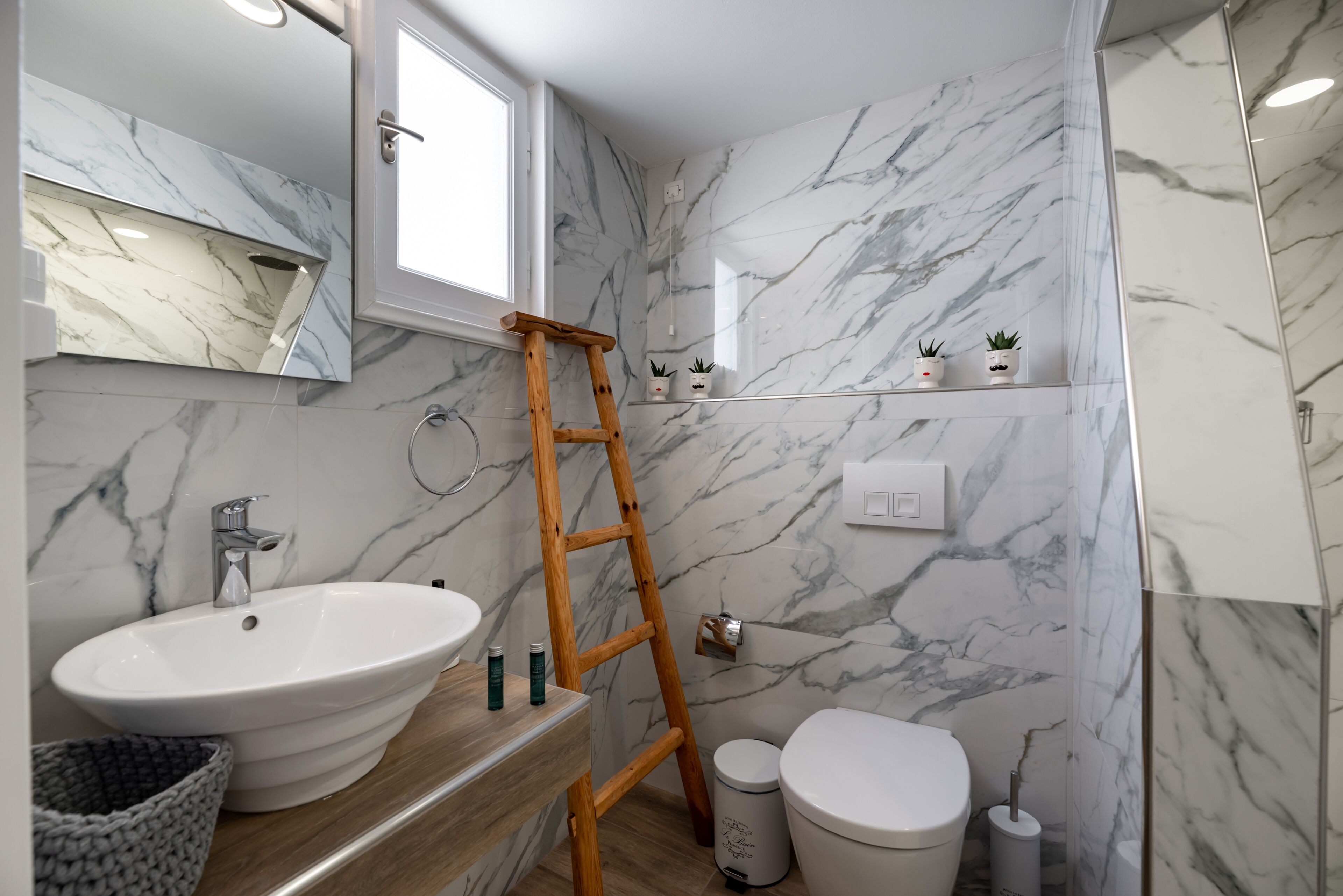 A bathroom with a marble wall, a wooden ladder, a sink, and a toilet.