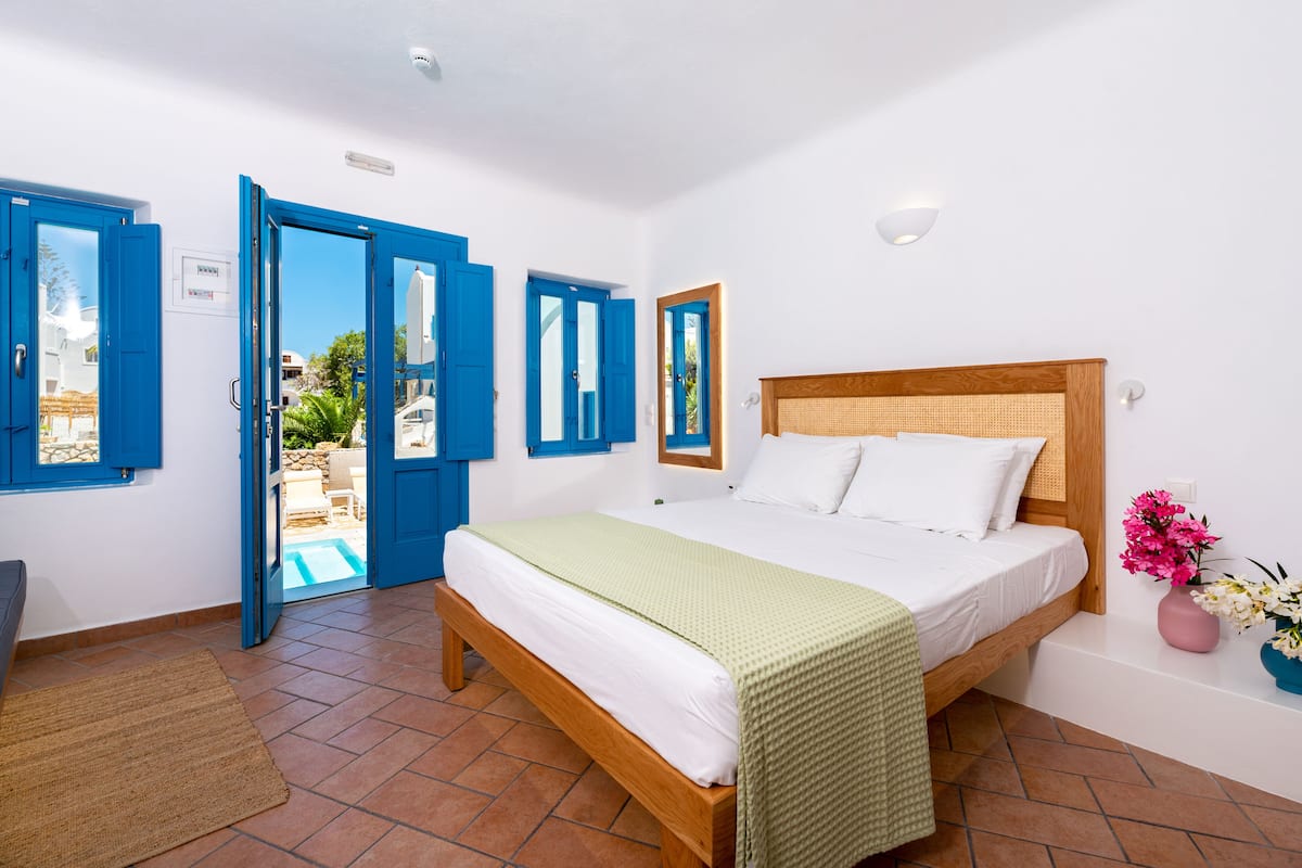 A bedroom with a wooden bed, white bedding, and blue doors leading to an outdoor area.