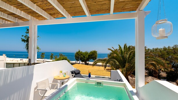 Una piscina en la azotea con vista al mar, paredes blancas y techo de madera.
