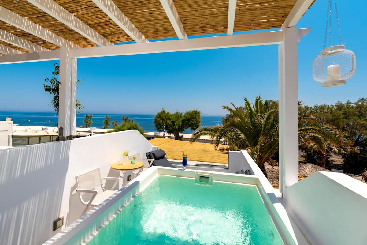 A rooftop pool with a view of the sea, white walls, and a wooden ceiling.