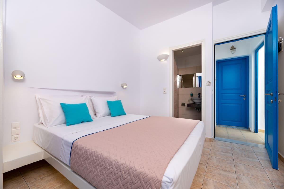 A bedroom with a bed, a nightstand, a blue door, and a bathroom visible through an open door.