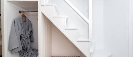A white interior with a wooden bench, a robe hanging on a rack, and a staircase.
