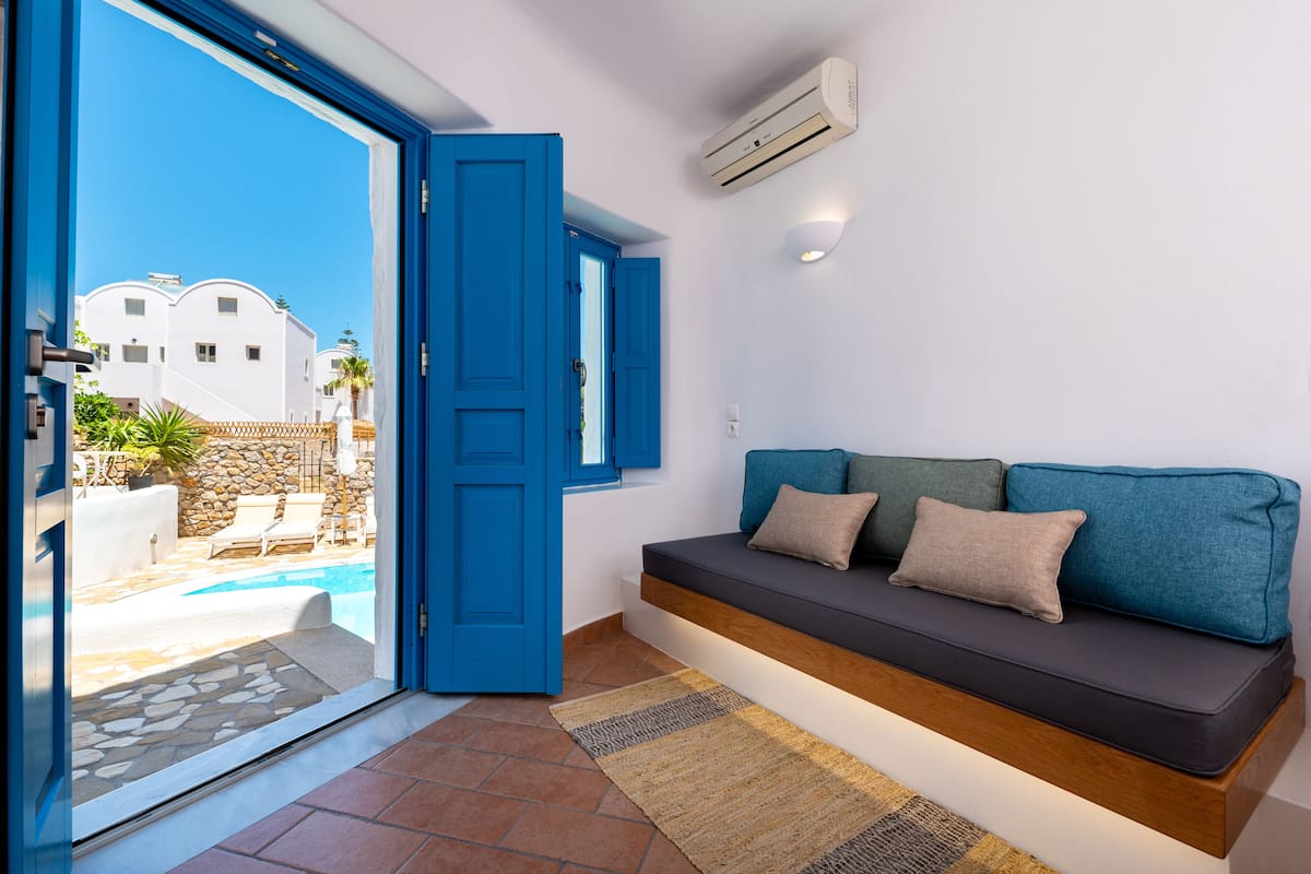 A modern living room with a blue door leading to a pool area, a built-in bench with cushions, and a stone wall.