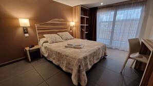 Una habitación de hotel con una cama grande, lámparas de noche, un escritorio y una silla.