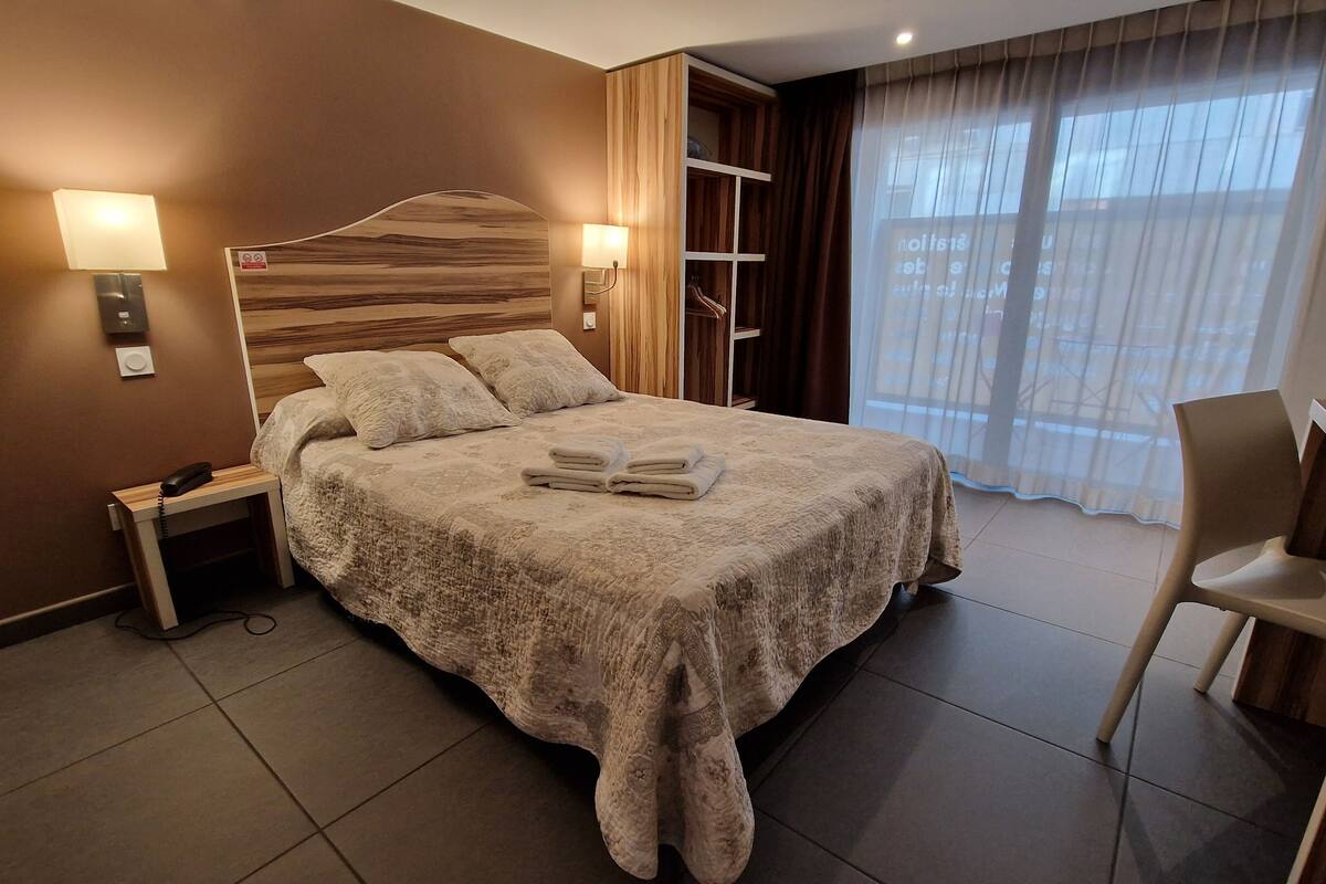 A hotel room with a large bed, bedside lamps, a desk, and a chair.
