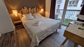 Una cama bien hecha con una colcha blanca y almohadas, un cabecero de madera y dos lámparas fijadas a la pared.