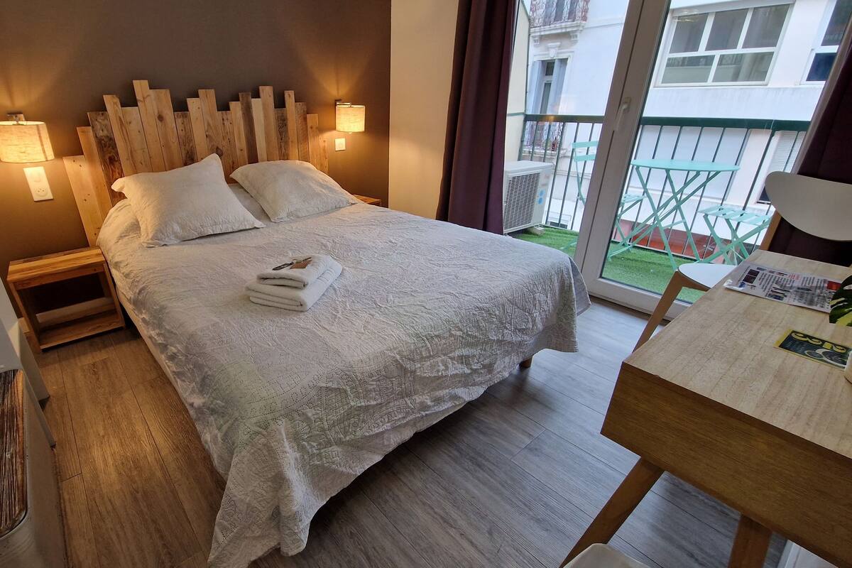 A neatly made bed with a white bedspread and pillows, a wooden headboard, and two wall-mounted lamps.
