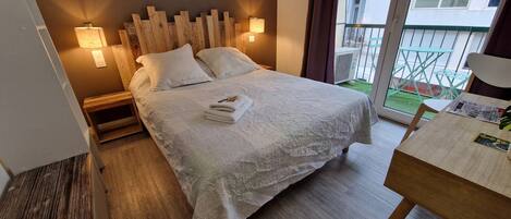 Una cama bien hecha con una colcha blanca y almohadas, un cabecero de madera y dos lámparas fijadas a la pared.