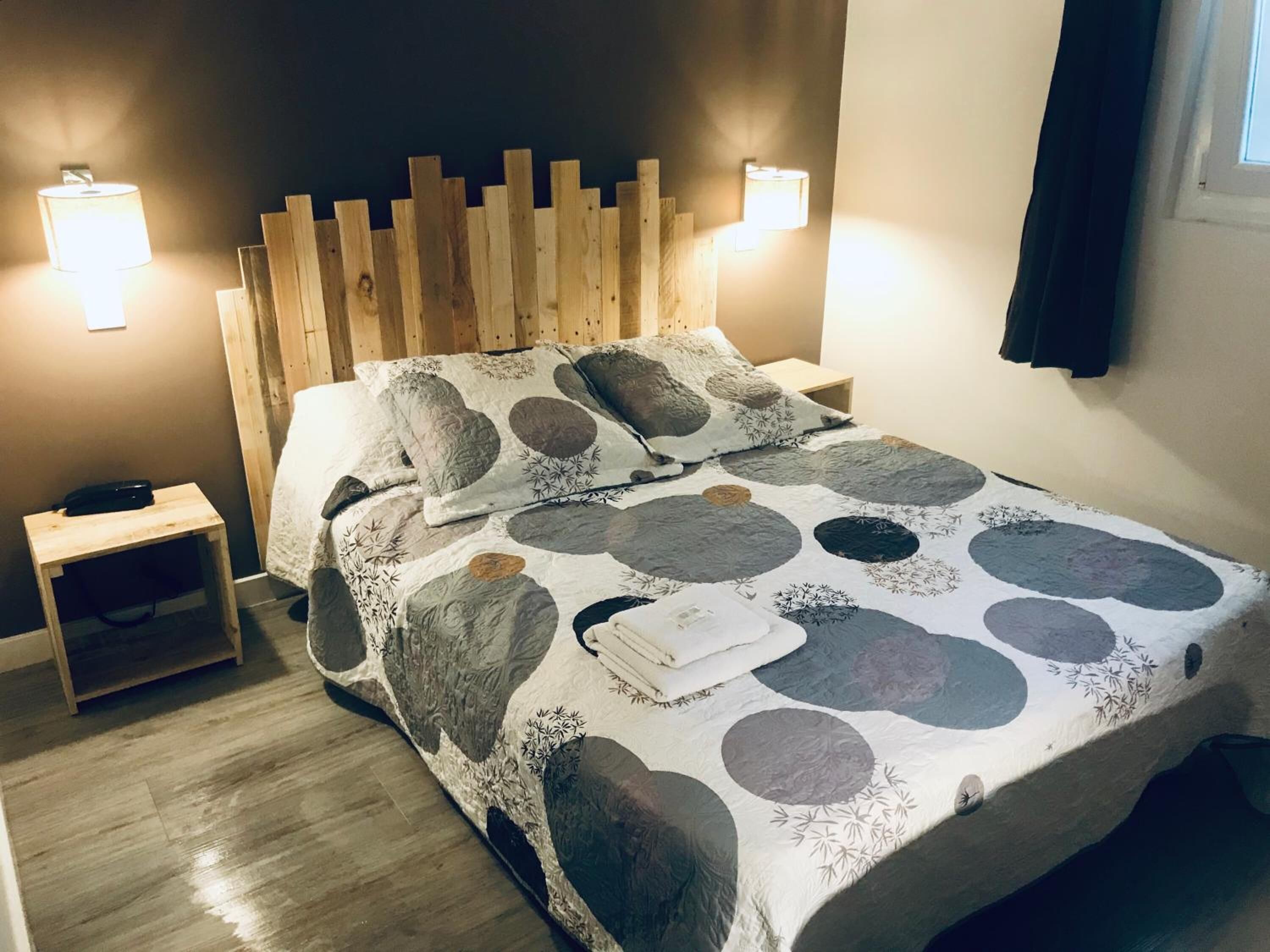 A neatly made bed with a patterned bedspread, two bedside tables with lamps, and a wooden headboard.