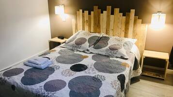 A bedroom with a wooden headboard, a bed with a circular patterned bedspread, two bedside tables, and wall-mounted lights.
