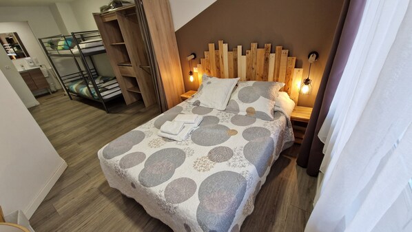 Une chambre à coucher avec un lit, une tête de lit en bois, des lampes de chevet et, au fond, un lit superposé.
