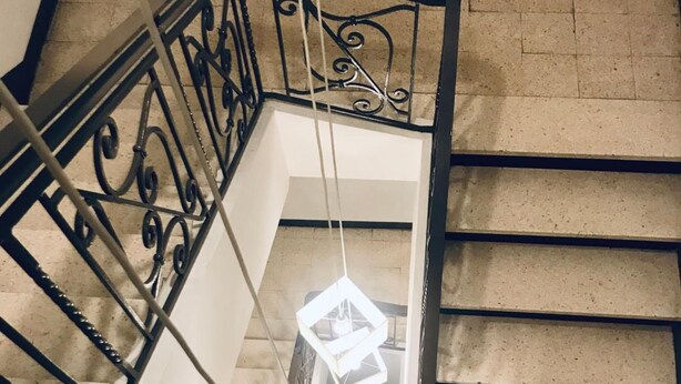 Una escalera con barandilla de metal negro y una lámpara colgante.