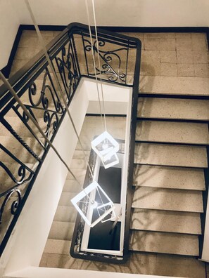 A staircase with a black metal railing and a hanging light fixture. - Hôtel Au Valéry (Sète)