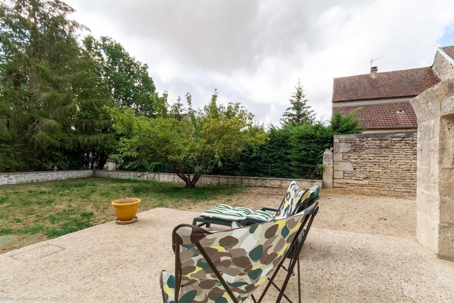 An outdoor seating area with a stone wall and a tree in the background.
