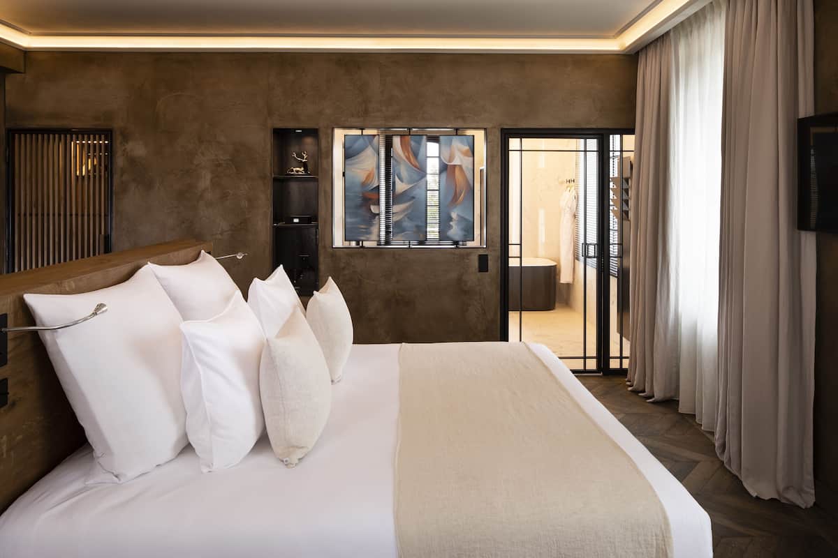 A modern hotel room with a large bed, a sliding glass door to the bathroom, and a mounted TV.