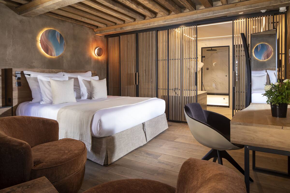 A modern hotel room with a large bed, a wooden ceiling, and a dining area with a table and chairs.