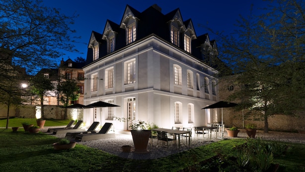 Un grand bâtiment illuminé, doté d’une façade symétrique, de nombreuses fenêtres et d’un jardin bien entretenu avec des espaces pour s’asseoir à l’extérieur.
