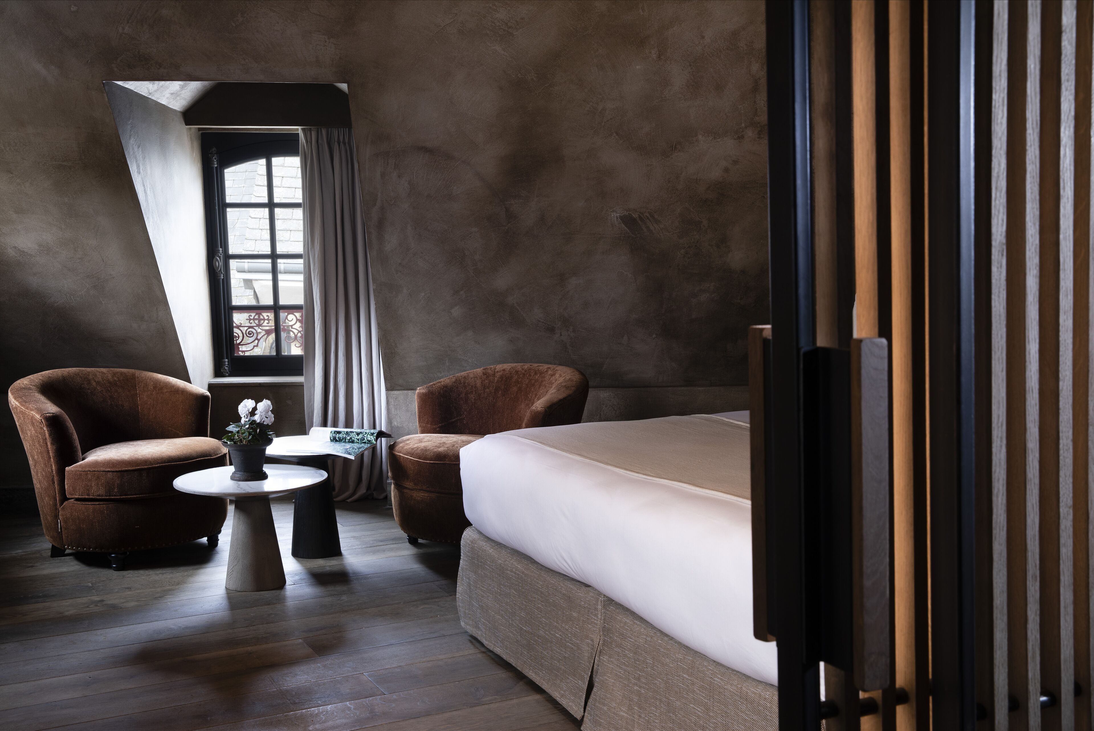 Una habitación de hotel moderna con una cama grande, dos sillones, una pequeña mesa redonda y una ventana con cortinas.