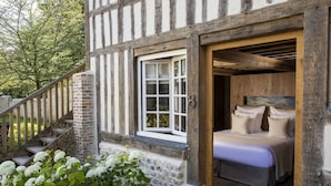 Il s’agit d’un bâtiment traditionnel à colombages, doté d’un escalier en bois, d’un lit avec une literie blanche et d’une fenêtre avec des volets blancs.