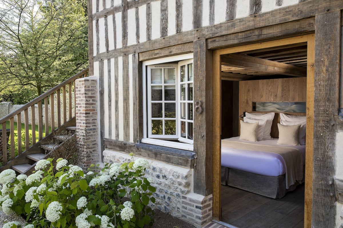 A traditional half-timbered building with a wooden staircase, a bed with white bedding, and a window with white shutters.