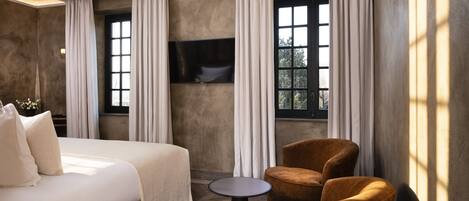 A hotel room with a large bed, two armchairs, a small table, and a TV mounted on the wall.