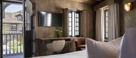 Un dormitorio con cama, escritorio, silla, televisor y vista al exterior.