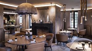 Un espace de restauration moderne avec des tables rondes, des sièges confortables, une cheminée et des luminaires suspendus.