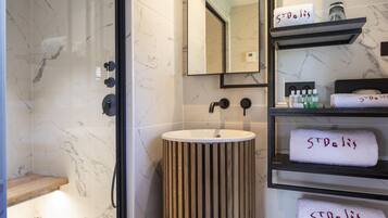 Un baño moderno con pared de baldosas de mármol, tocador de madera, un lavamanos y estantes con toallas etiquetadas "ST. Deli".