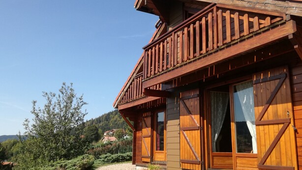 Ein Holzhaus mit Balkon, großen Fenstern und Blick auf ein bewaldetes Gebiet.