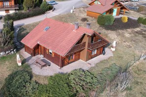 A wooden cabin with a red roof, a balcony, and a gravel driveway.