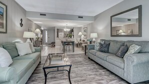 A spacious living room with two sofas, a coffee table, and a dining area with a chandelier. - Sonrise Retreat - Hosted By Moore AI Rentals (Fernandina Beach)