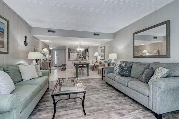 A spacious living room with two sofas, a coffee table, and a dining area with a chandelier.