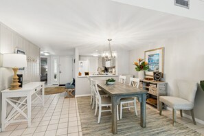 A modern kitchen with white cabinetry, a dining area with a wooden table and chairs, and a living space with a sofa and a coffee table.