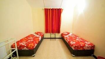 A small, narrow room with two single beds, each with a floral bedspread. There is a ladder against the wall, and a red curtain hangs at the end of the room.