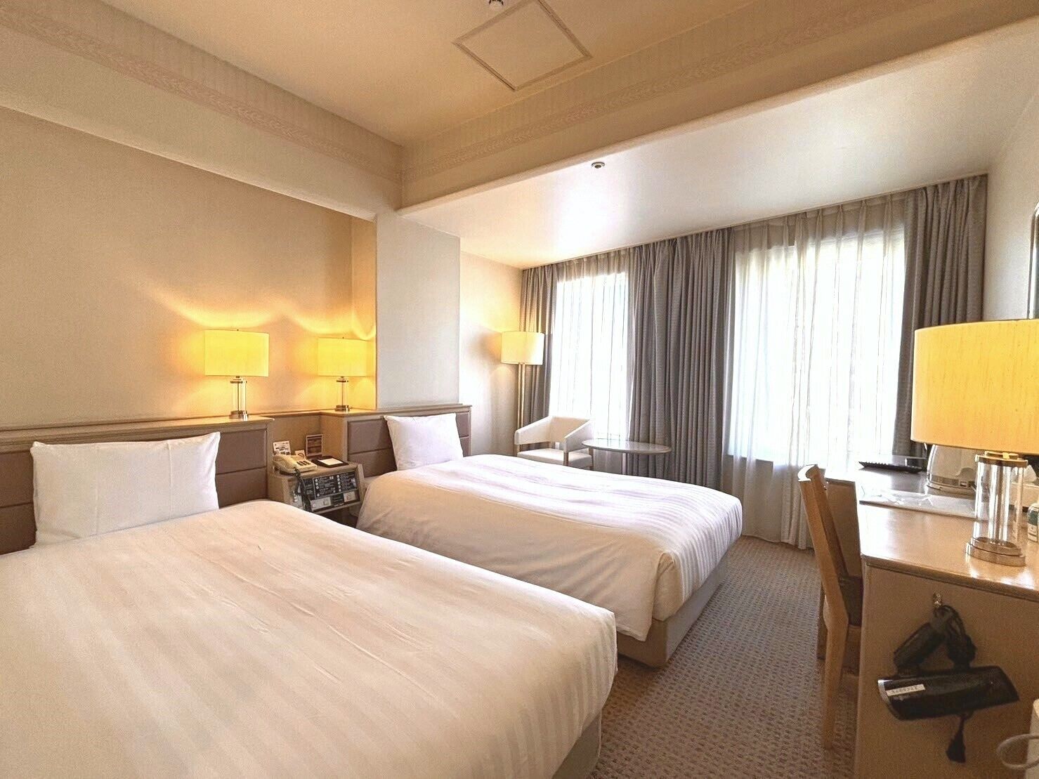 A hotel room with two beds, a desk, a chair, and a small table.
