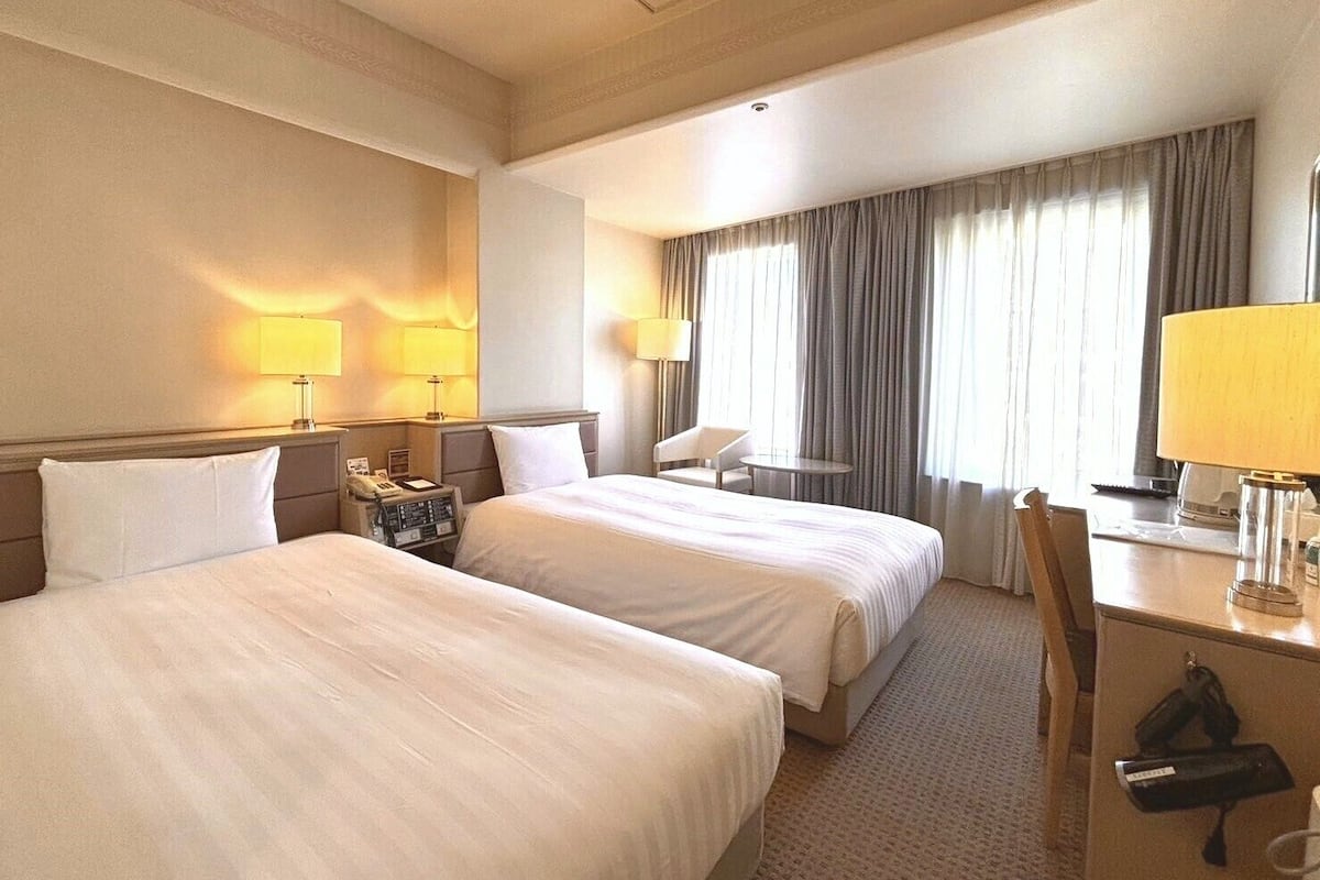 Habitación de hotel con dos camas, un escritorio, una silla y una mesita.