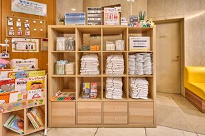 Een hotel receptie met een houten toonbank, een prikbord met verschillende berichten, en een geel bankje.