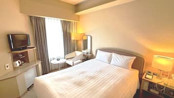 A hotel room with a bed, a TV on a stand, a desk with a chair, a lamp, and a telephone.