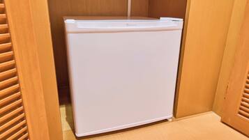 A compact white refrigerator in a wooden cabinet with a wooden floor.