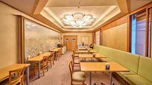 Habitación de hotel con comedor que incluye mesas y sillas de madera, un sofá verde y una lámpara decorativa en el techo.