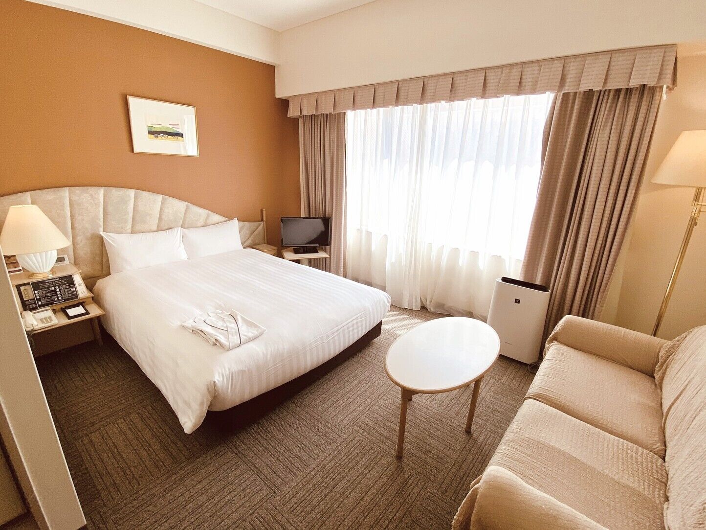A hotel room with a bed, bedside table, TV, and a small round table.