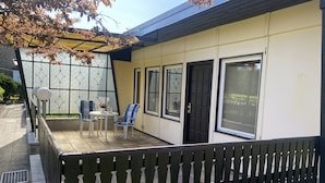 Een overdekt terras met een tafel en stoelen, een zwarte deur en grote ramen.