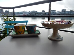 Mesa com duas chávenas coloridas e uma taça de petiscos, com vista para a água e edifícios.