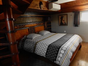 Quarto com cabeceira de madeira, cama com roupa de cama estampada, escada, quadro na parede e ar condicionado.