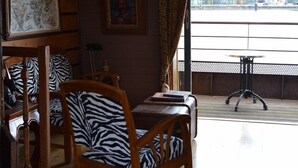 Zona pranzo con arredi in legno e cuscini a motivi zebrati, un quadro appeso alla parete e vista sugli edifici attraverso un'ampia finestra.