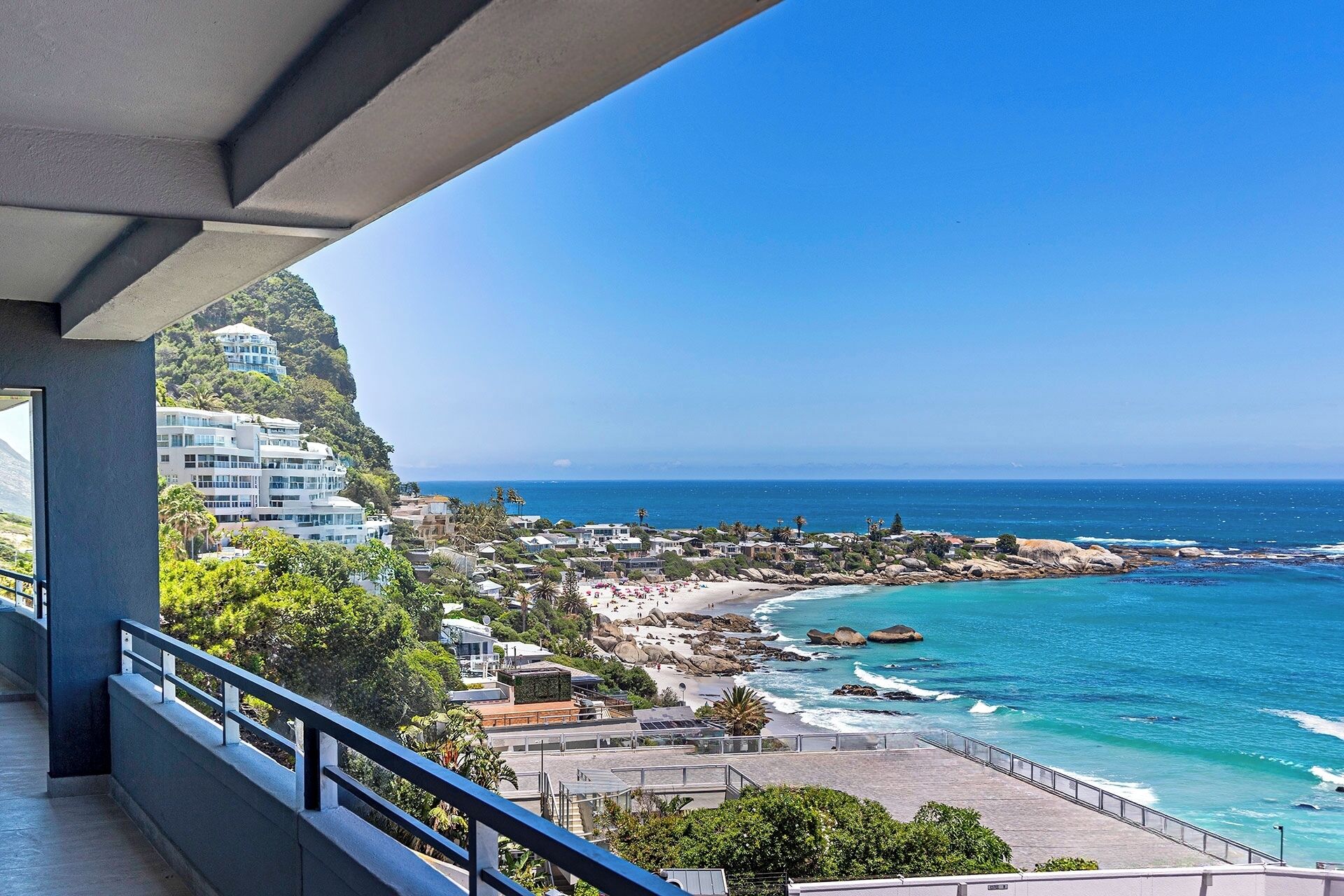 Blick aufs Meer vom Balkon, der auf einen Strand mit klarem, blauem Wasser und einer felsigen Küste blickt.