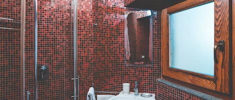 Ein Badezimmer mit roten Mosaikfliesen, einem Holzrahmenfenster, einem weißen Waschbecken und einer Duschkabine aus Glas.