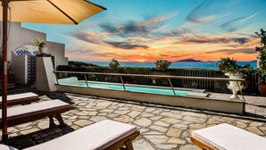 A stone patio with lounge chairs and a pool, overlooking a scenic sunset view. - Lubra Casa Relax (Massa lubrense)